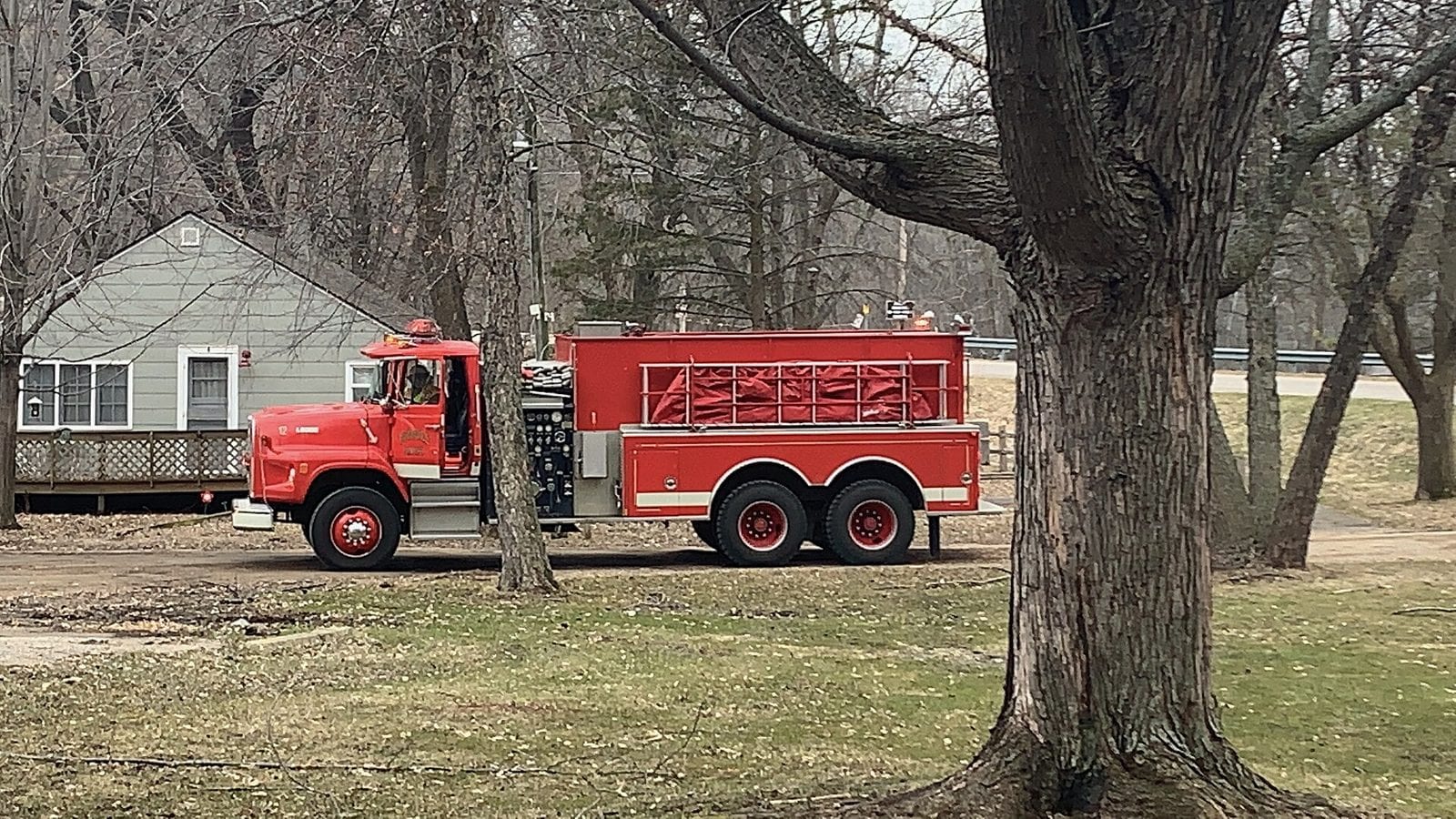 A red tanker-pumper parked on the grass beneath bare trees in late autumn.